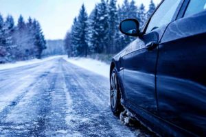 A black car on an iced road surrounded by trees covered with snow
